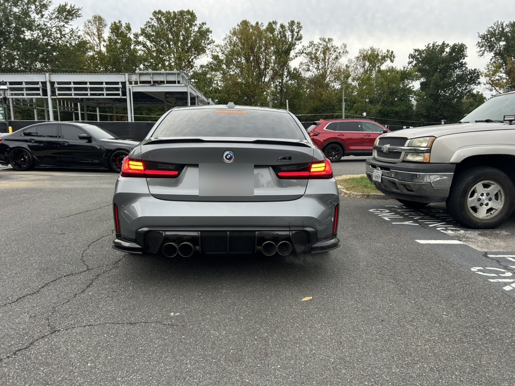 Quad outlets through a carbon rear diffuser, trunk lip spoiler. Plate blurred.
